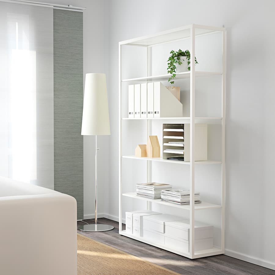 White shelf positioned against a wall, displaying stacks of magazines, boxes and a faux plant