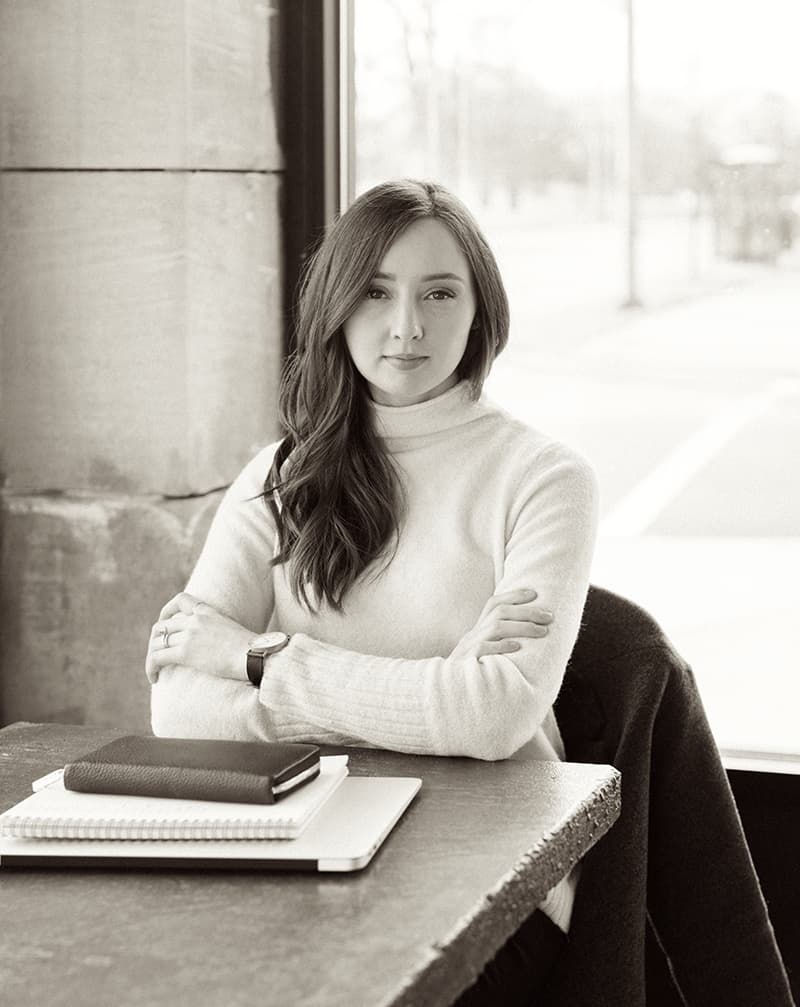 Woman sitting at a table, lightly crossing her arms and staring at the camera