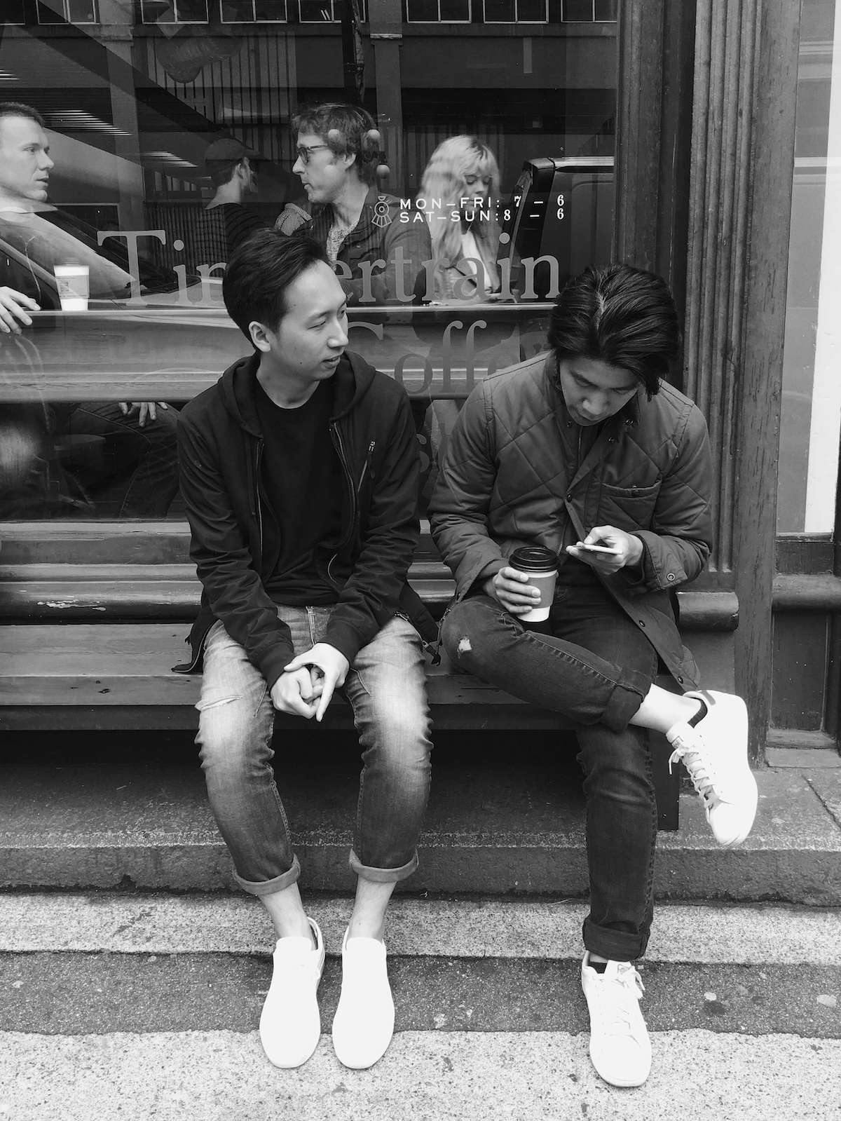 Two friends sitting on a bench outside of a coffee shop